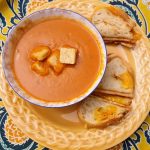 bowl of cream of tomato soup topped with croutons and side of grilled cheese