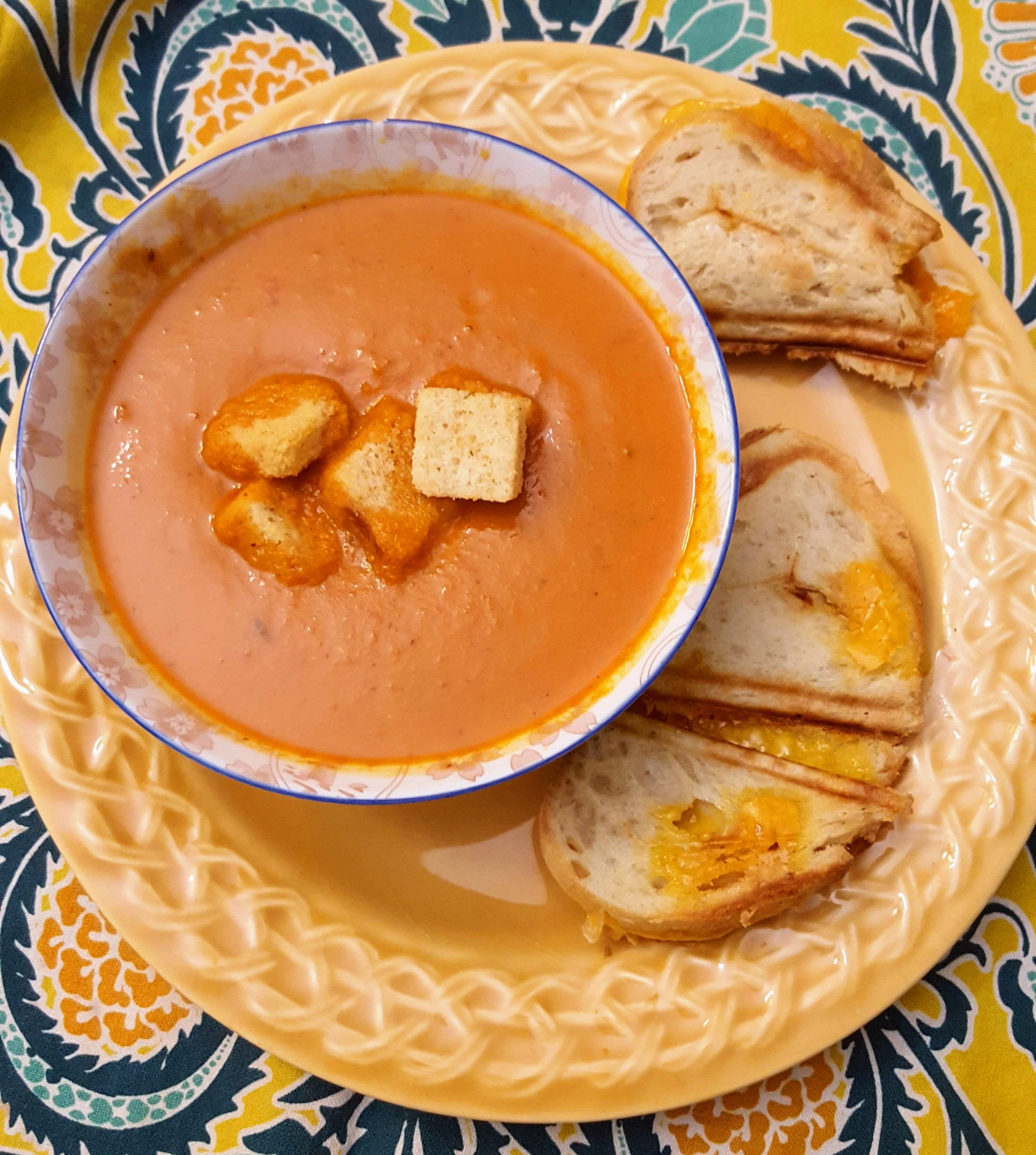 bowl of cream of tomato soup topped with croutons and side of grilled cheese