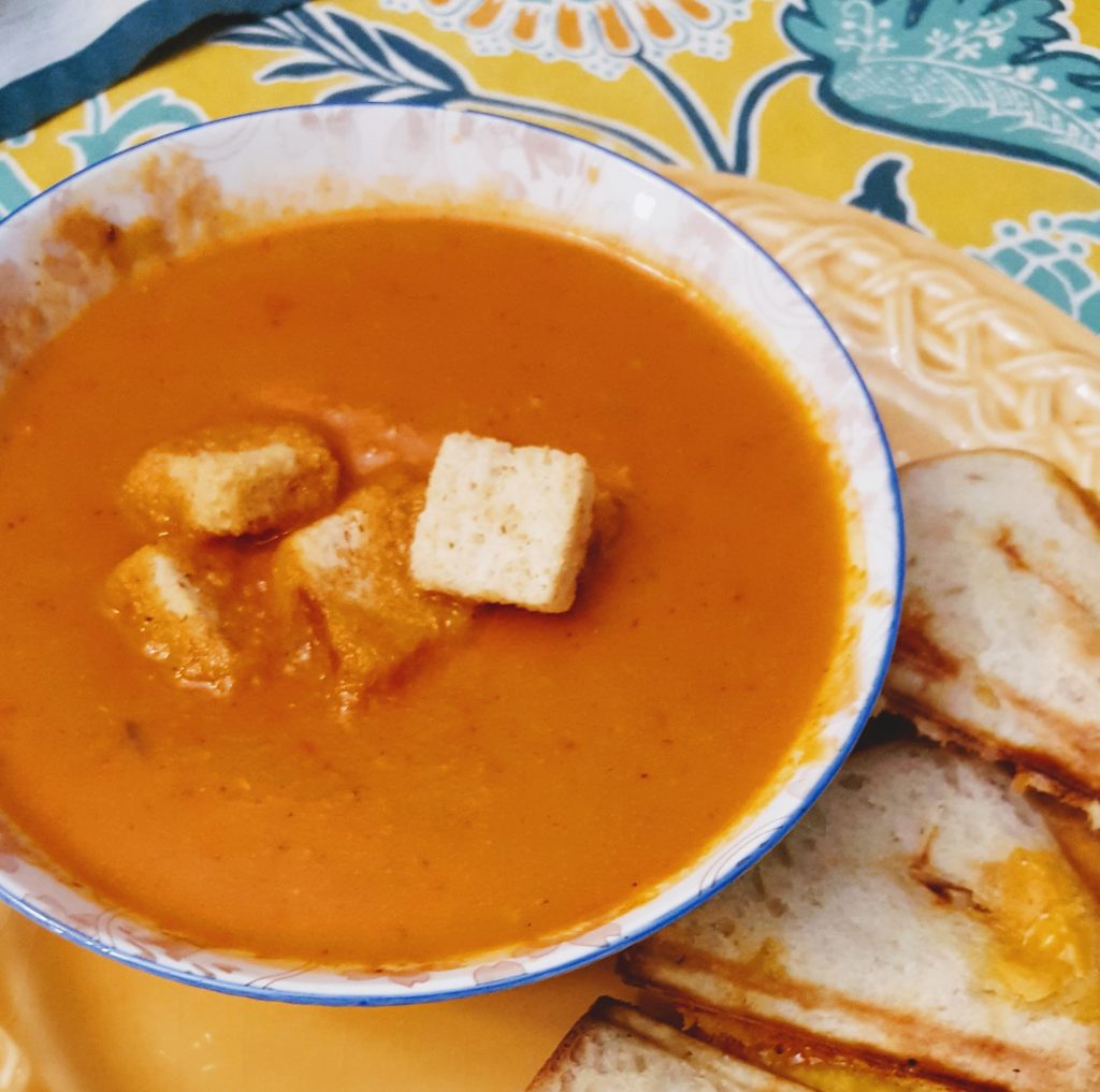 bowl of cream of tomato soup topped with croutons and side of grilled cheese