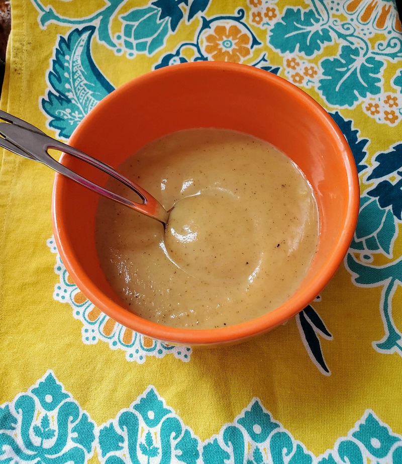 spicy curry soup in an orange bowl on top of a yellow print tablecloth