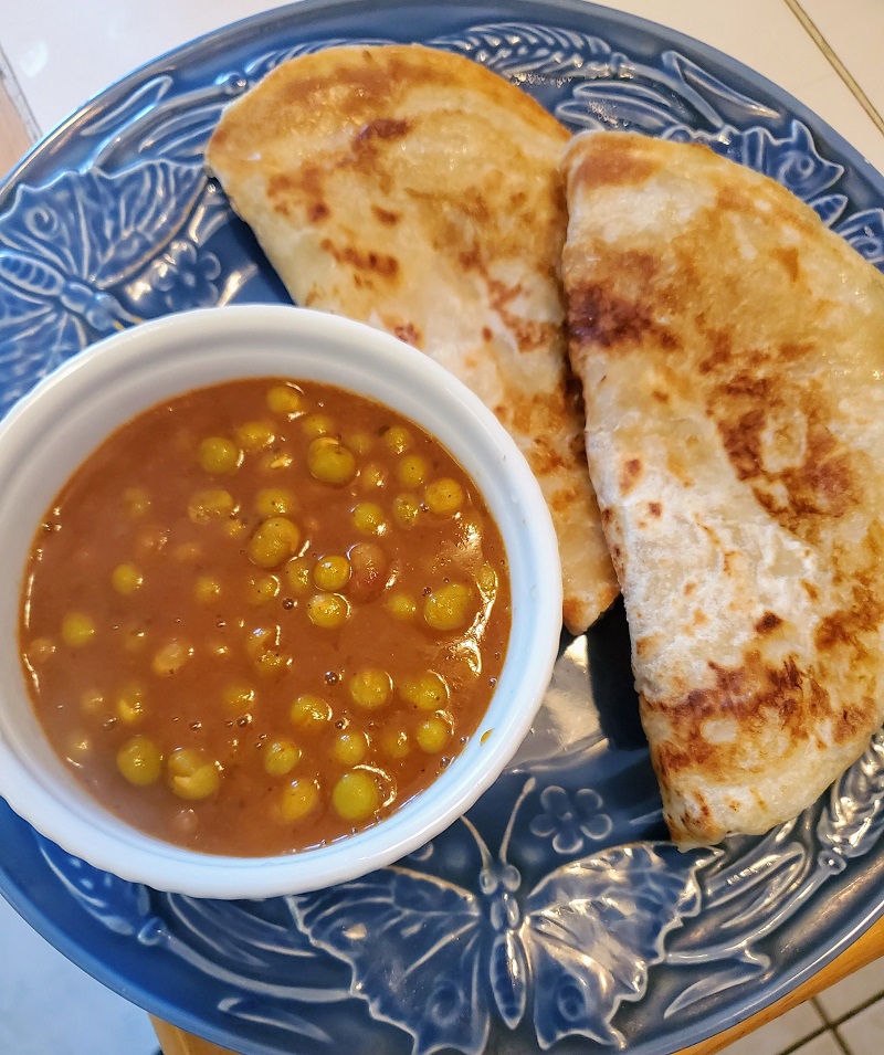 bowl of pigeon peas and paratha flatbread on a blue plaate