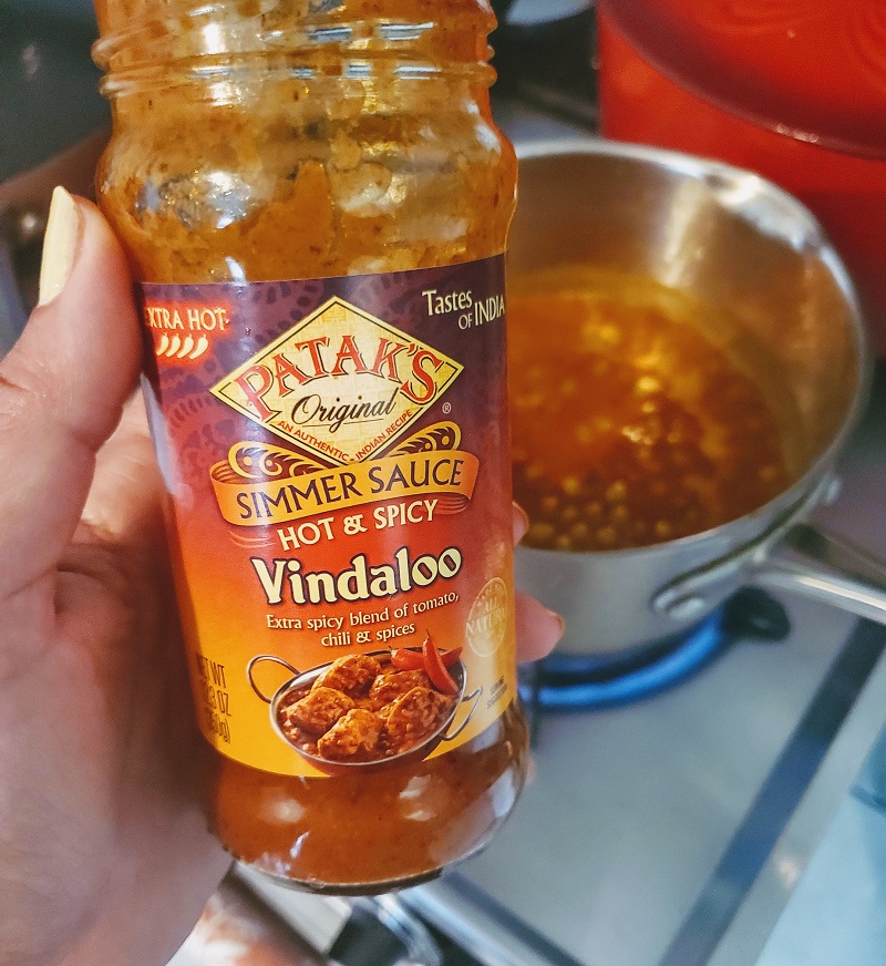 jar of Patak's Vindaloo simmering sauce in front of a pot of pigeon peas