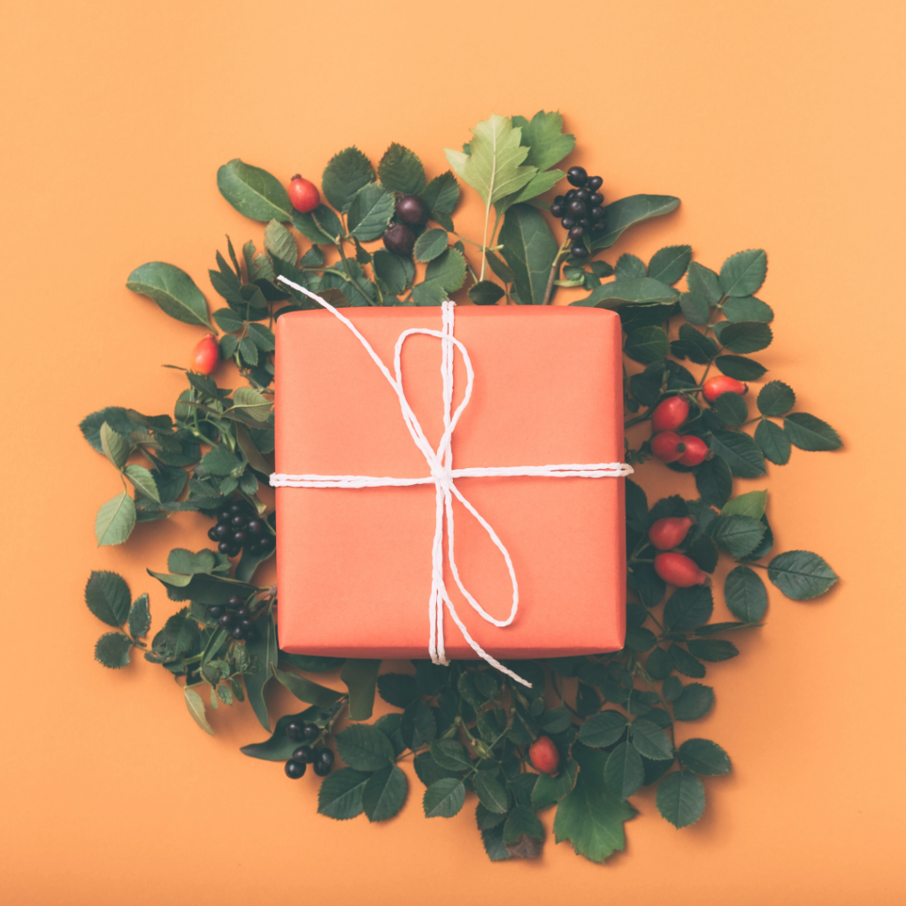 orange package tied with raffia bow on top of holiday wreath